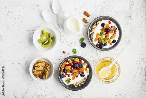Breakfast, rice porridge or natural yoghurt with assorted berries, fruits and nuts: kiwi, pomegranate, blueberries, almonds, dried apricots in small bowls on a light background. Top view. Copy space.