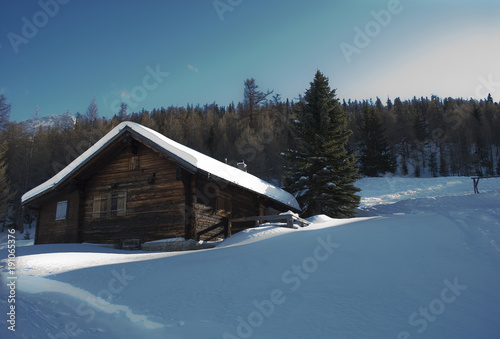 small wooden mountain hut (cabin), old, covered by snow, high mountain, struck by a ray of sunshine, sunset, forest, isolated, fairytale, winter, Alps, Rothwald, Switzerland © Angela