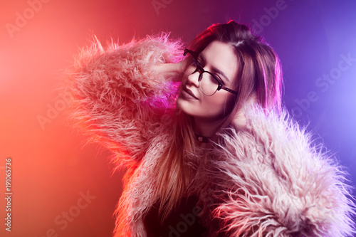 Fashionable young woman in a fluffy pink coat, neon light. Portrait of a beautiful trendy girl