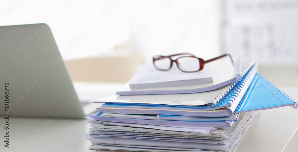Laptop with stack of folders on table on white background Laptop with stack of folders on table on white background