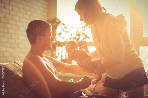 Portrait of young happy man and woman holding newborn cute babe . Caucasian smiling father and mother embracing tenderly adorable new born child. Happy family concept . Art warm light.