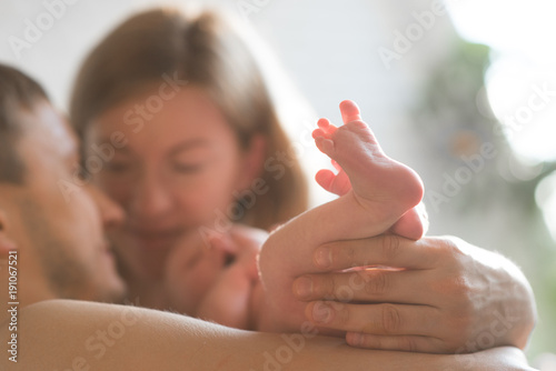 The focus on newborn's legs . Caucasian smiling father and mother embracing tenderly adorable new born child. Happy family concept.Deadpan raw photo nofilter