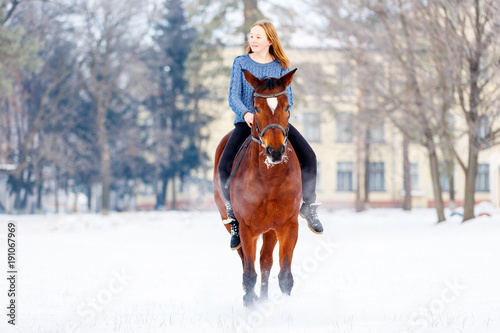 Young teenage girl riding on her bay horse in winter park