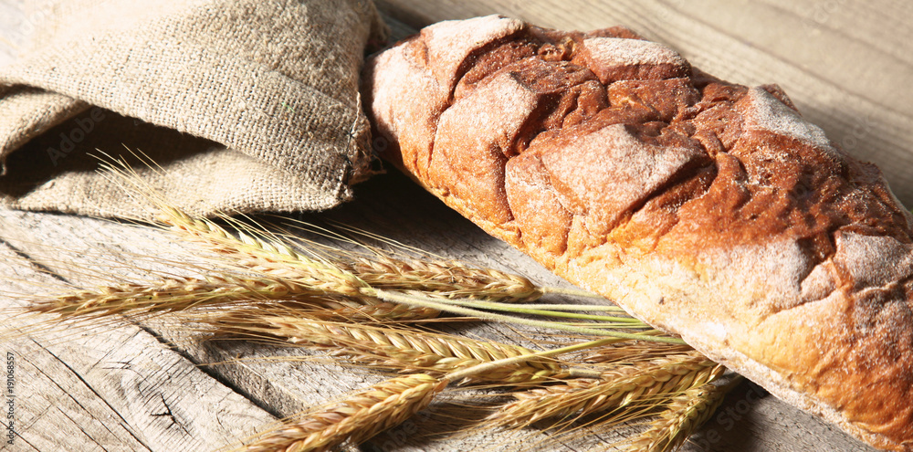 rustic crusty bread and wheat ears on a dark wooden table