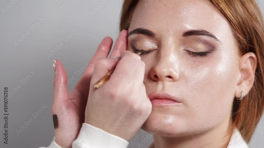 portrait of a young and beautiful woman who is waiting for the end of make-up, a professional dark make-up artist applies eyeliner to her eyes portrait of a young and beautiful woman who is waiting for the end of make-up, a professional dark make-up artist applies eyeliner to her eyes