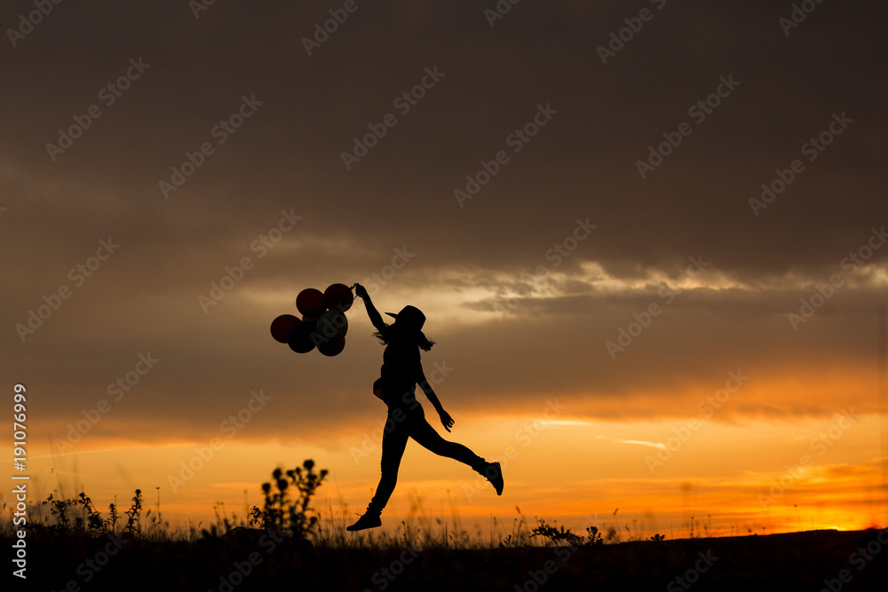 silhouette of a young woman jumping at sunset. Outdoors. She is holdings balloons. Fun and lifestyle