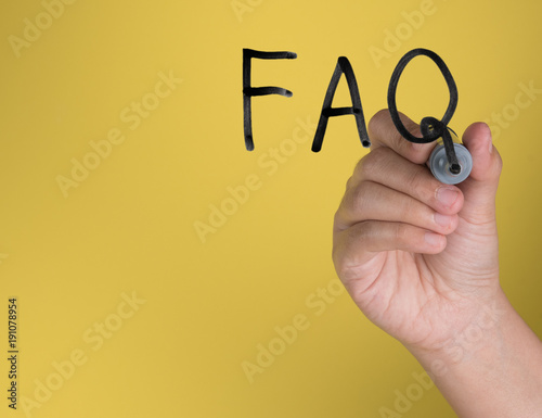 Hand holding black permanent marker and writing word "FAQ"against yellow background