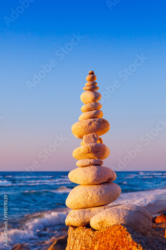 Rock zen pyramid of white stones in the pink rays of the setting sun against the sea