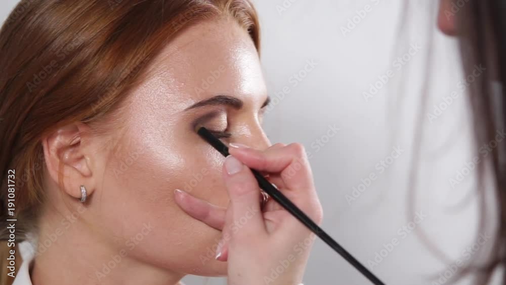 close up shot of the face of a young and beautiful woman, the make-up artist applies with the help of a brush a shadow on the upper eyelid of the eye close up shot of the face of a young and beautiful woman, the make-up artist applies with the help of a brush a shadow on the upper eyelid of the eye