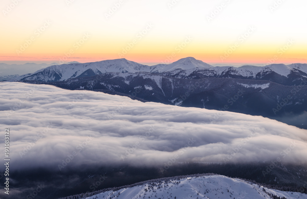 Sunset view of snowy mountain ranges with low clouds in the foreground