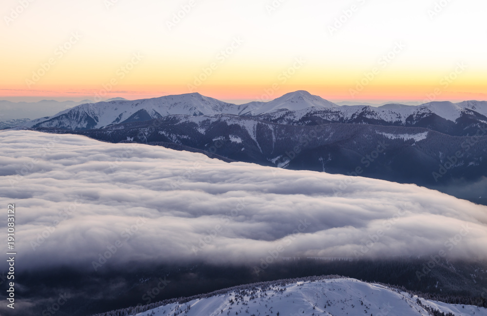 Obraz premium Sunset view of snowy mountain ranges with low clouds in the foreground