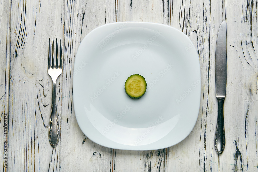 Eating for a girl, women on a strict diet. Two little funny green cucumber with pimples on a white plain plate. Too little food for losing weight. Anti-obesity diet by evil nutritionist.
