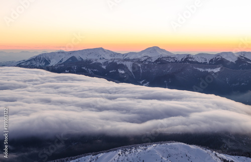 Sunset view of snowy mountain ranges with low clouds in the foreground
