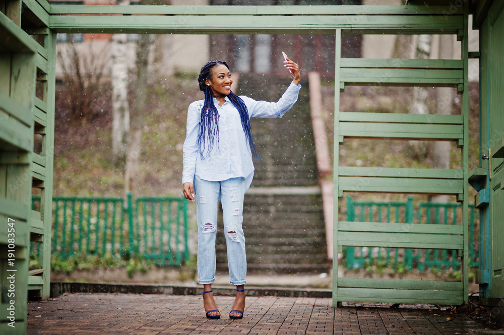 Stylish african american girl with dreads holding mobile phone at hand, outdoor snowy weather.