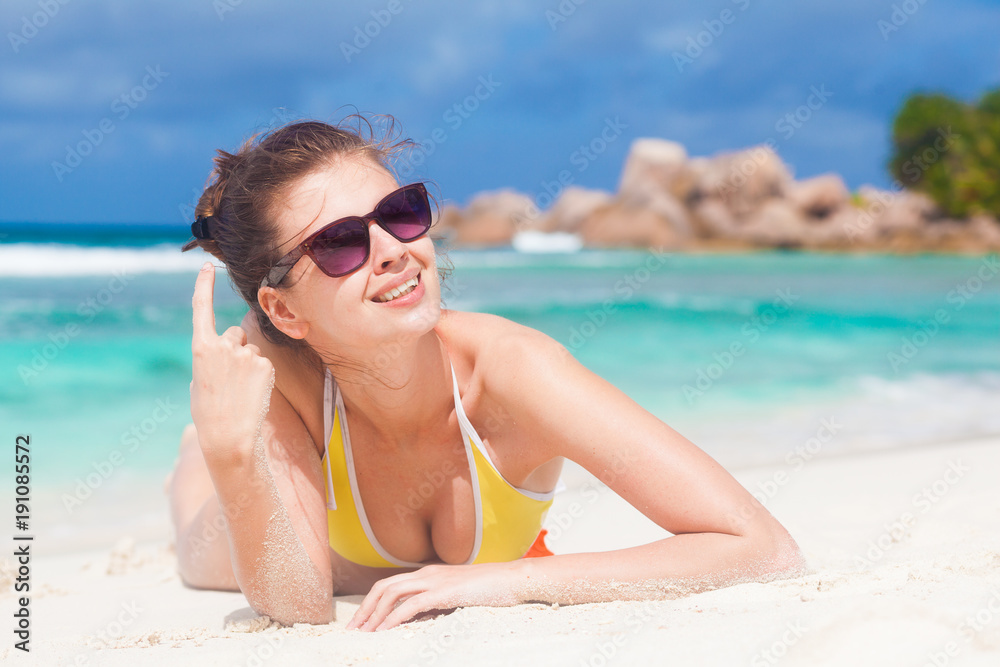 portrait of long haired woman in bikini and sunglasses lying on tropical beach. La Digue, Seychelles