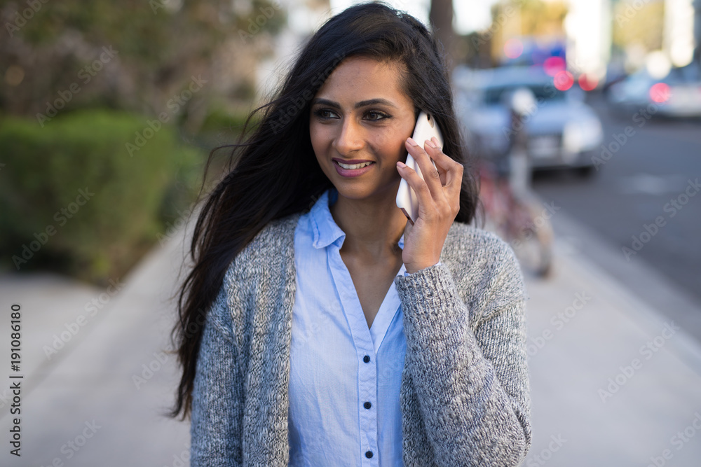 Fototapeta premium Young Indian woman walking street talking on cell phone