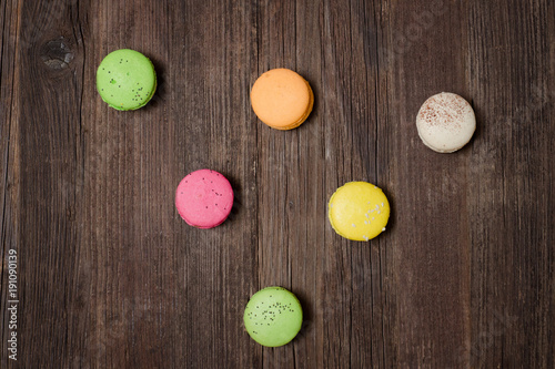 Six multicolored macarons on a brown wooden table. Top view