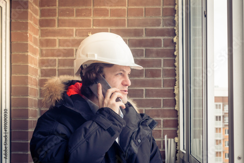 Young civil engineer is having trouble over the phone against brick background. Soft focus, toned. photo