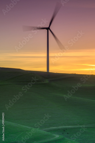 Photography Lone wind turbine spinning on a grassy hillside sunset