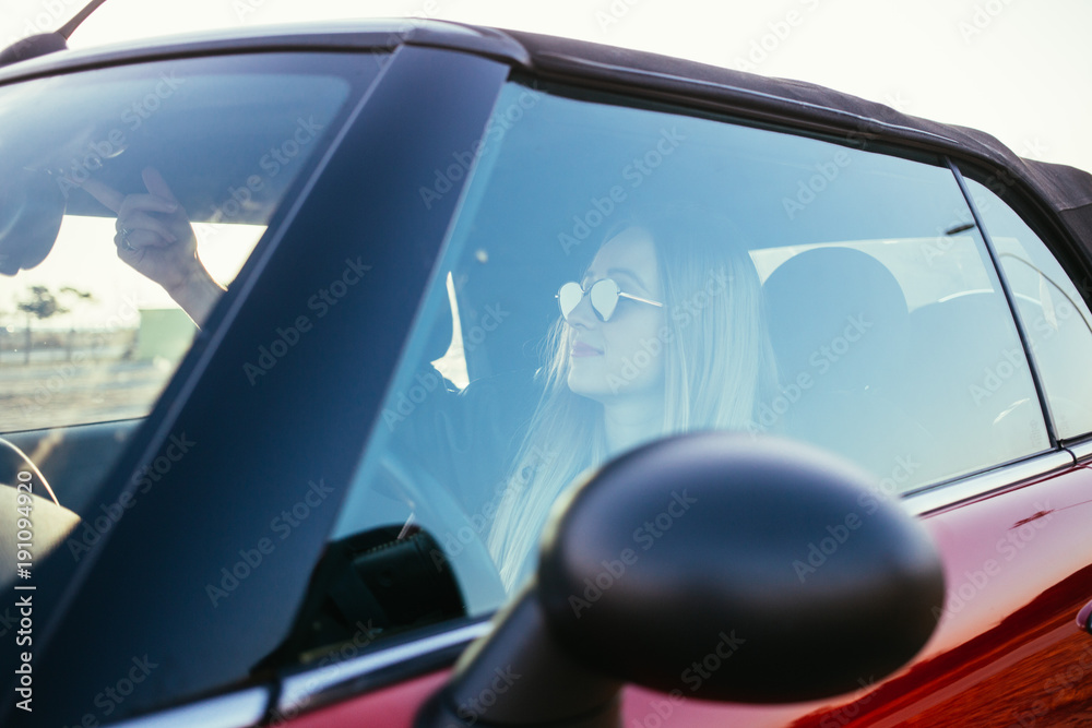 Attractive and beautiful natural confident and empowered young woman with blonde hair opens roof of convertible cabriolet at sunset car park,ready to ride into summer vacation or holiday.forever young