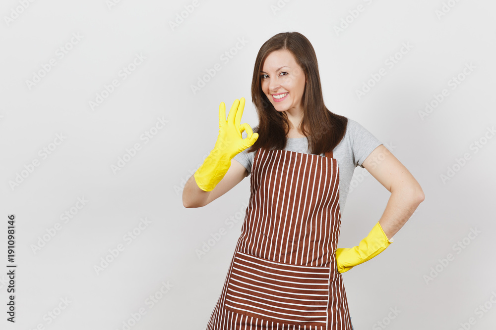 Young attractive smiling brunette housewife in striped apron, yellow gloves isolated on white background. Beautiful housekeeper woman showing OK gesture looking camera. Copy space for advertisement. Young attractive smiling brunette housewife in striped apron, yellow gloves isolated on white background. Beautiful housekeeper woman showing OK gesture looking camera. Copy space for advertisement.