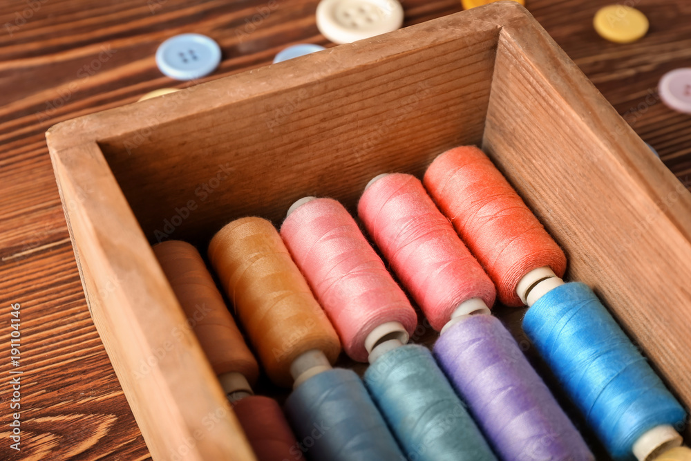 Wooden box with color sewing threads on table, closeup Wooden box with color sewing threads on table, closeup