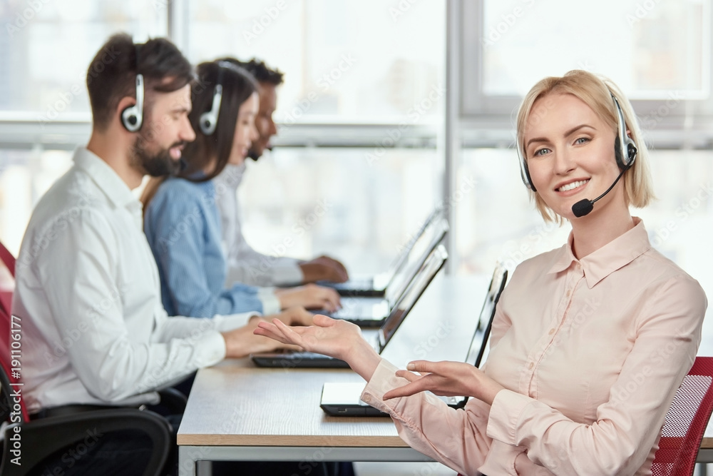 Female operator recommeding her co-workers. Lady with headset in call center office pointing at her colleagues using both hands. Female operator recommeding her co-workers. Lady with headset in call center office pointing at her colleagues using both hands.