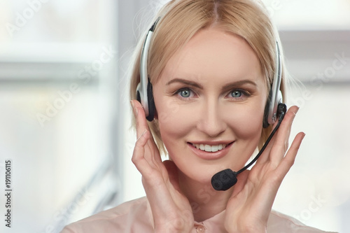 Front view mature woman's face with headset. Portrait of blond lady touching headset using both hands.