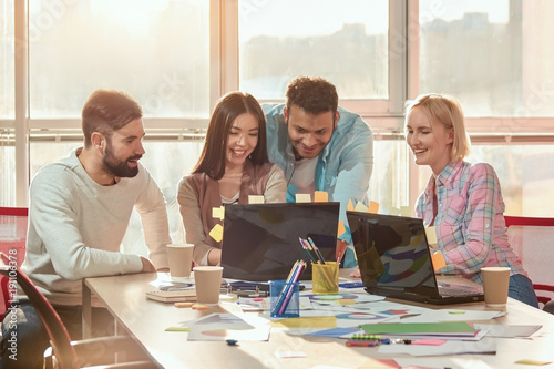 Designers gladly looking at laptop screen. Group of friends and colleagues are watching funny videos during break at work. photo