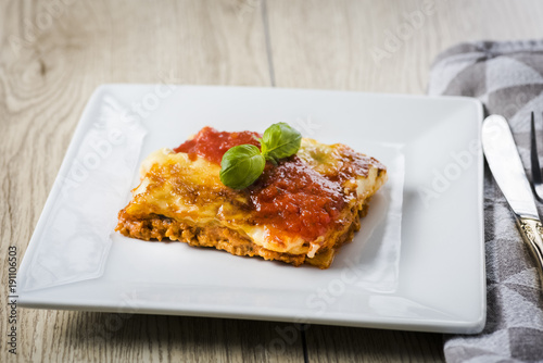 appetizing portion of lasagna on a white plate with tomato sauce