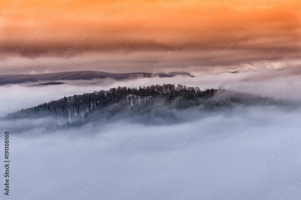 Winter foggy mountain landscape. Fairytale sunset with dramatic clouds in the orange sky