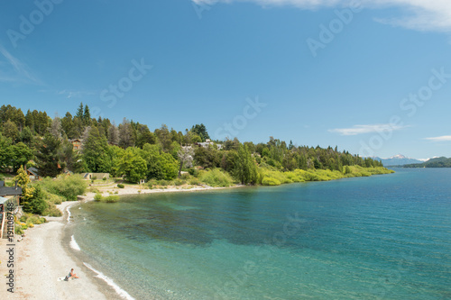 Costa frente a lago turquesa con bosque de fondo y cielo azul