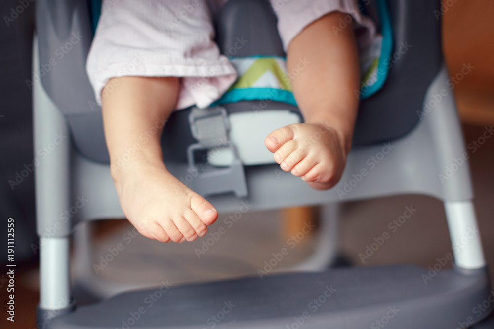 Closeup of adorable chubby baby legs feet. Small kid sitting in high chair. Macro detail of cute child