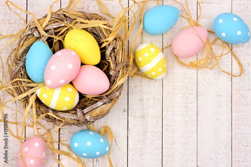 Springtime nest with pink, yellow and blue painted Easter Eggs. Corner border against a rustic white wood background.