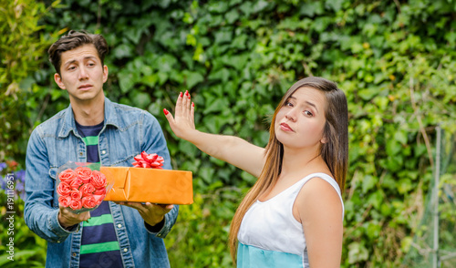 Close up of blurred man holding a gift and flowers with shocked face after see his girlfriend stretching her arm ignoring him , friendzone concept