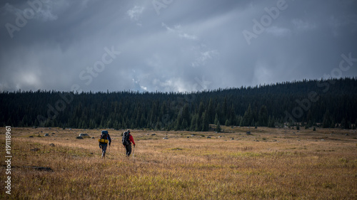Two hikers walking through field in front of storm clouds © Braeden