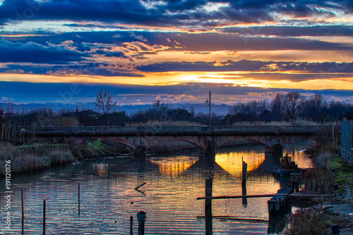 sunset on river under  ancient railway bridge photo