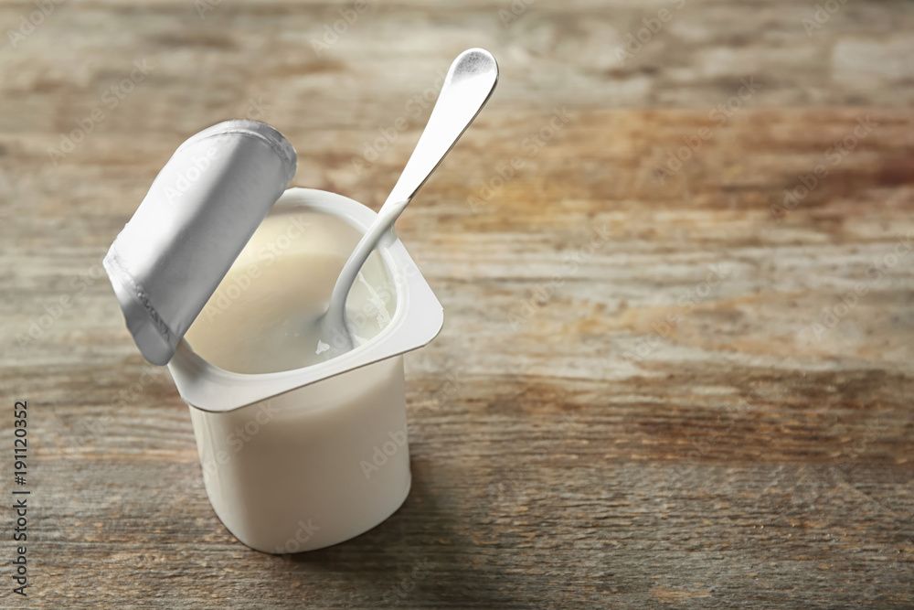 Plastic cup with yogurt on wooden background