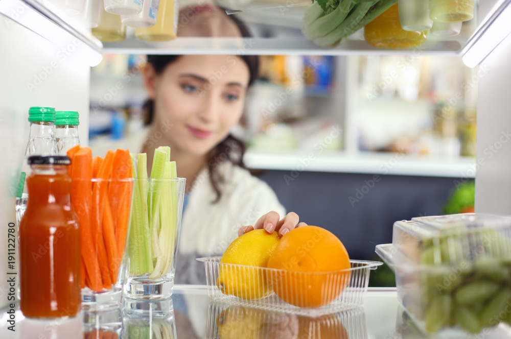 Portrait of female standing near open fridge full of healthy food, vegetables and fruits. Portrait of female