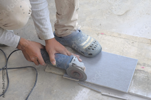 Worker cutting floor tiles with angle grinder at construction site