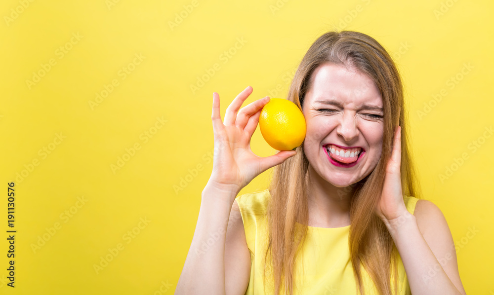 Happy young woman holding a lemon on a yellow background Happy young woman holding a lemon on a yellow background
