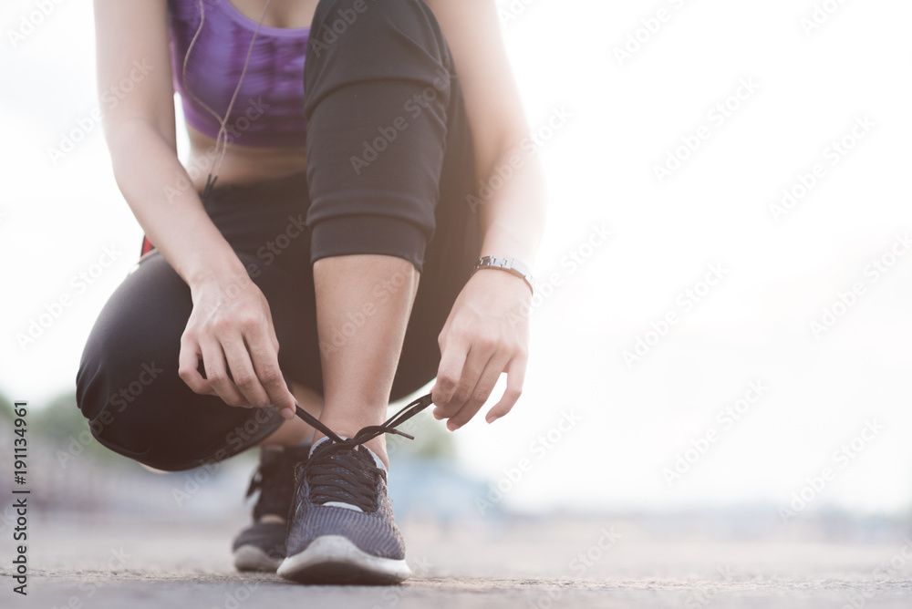 young woman runner tying shoelaces before jogging standing on footpath.
