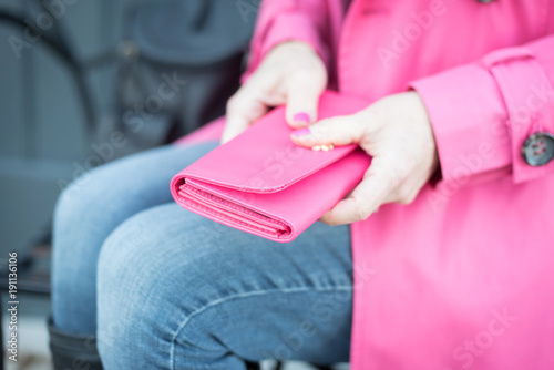 woman sitting on bench holding pink wallet