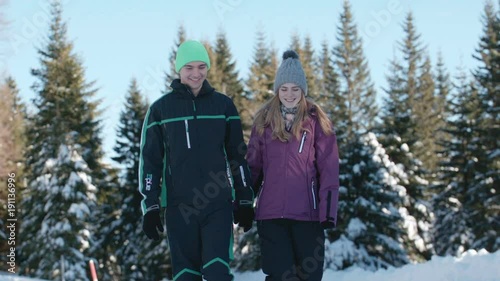 Young couple walking on a snowy path in the middle of a forest on a sunny day