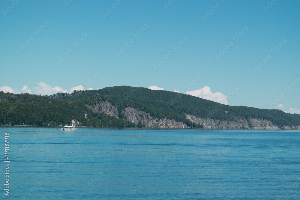 Landscape of a blue lake with catamaran going on and mountains in the background