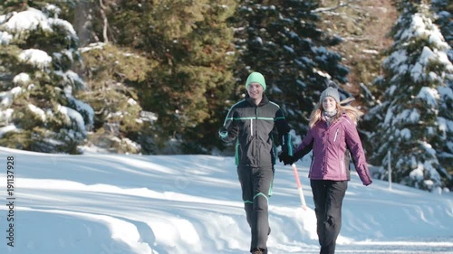 Young couple running along a snowy path in the middle of a forest on a sunny day
