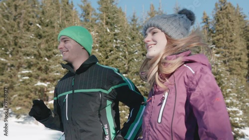Young couple running along a snowy path in the middle of a forest on a sunny day