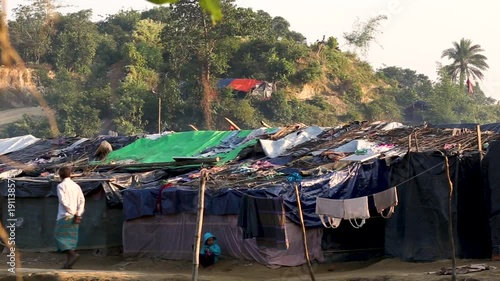 A man walks on a dirt road next to some small tin houses in a refugee camp photo