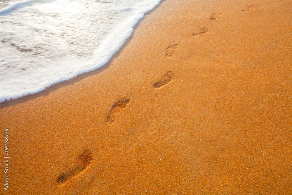 beach, wave and footprints at sunset time