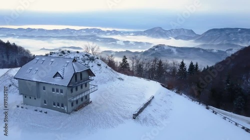 Aerial show of snowy day including cottage and mountains surrounded by fog